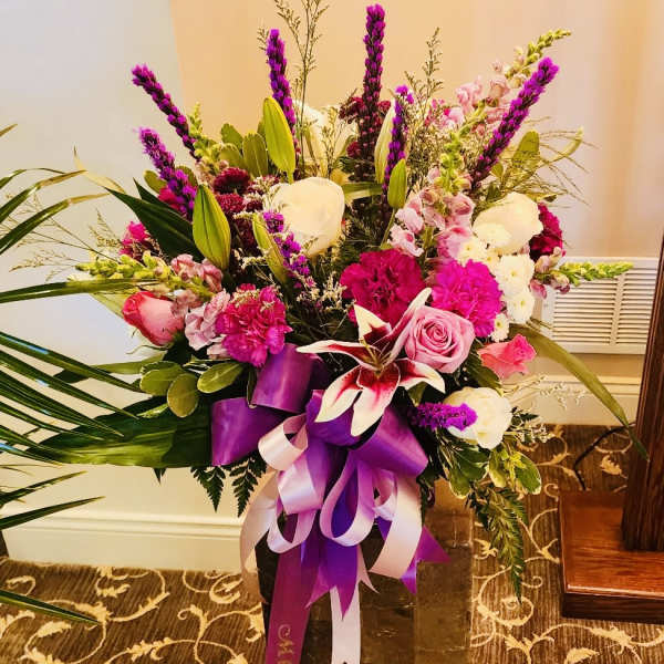 Tall bouquet of pink, white, and purple flowers in a dark vase with ribbon