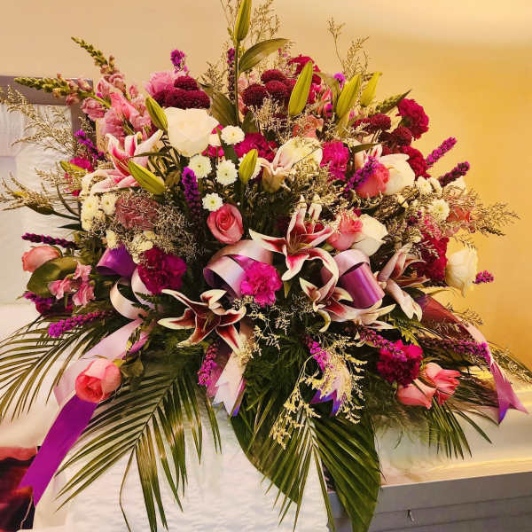 Large pink and white floral spray with ribbons on a casket