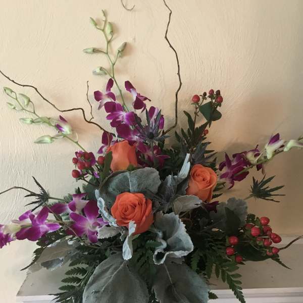 Arrangement of orange roses and purple orchids in a low container