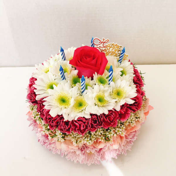 Round birthday cake made of flowers with a red rose and candles