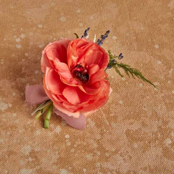 Coral ranunculus boutonniere with small purple accents