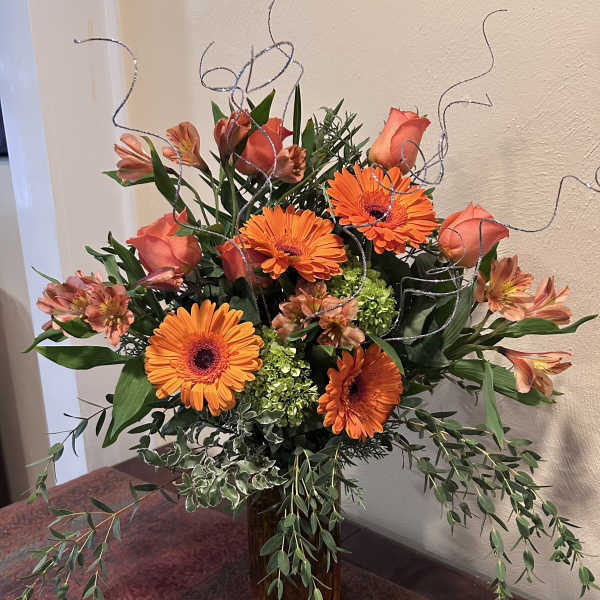 Orange gerbera daisies and roses in a glass vase