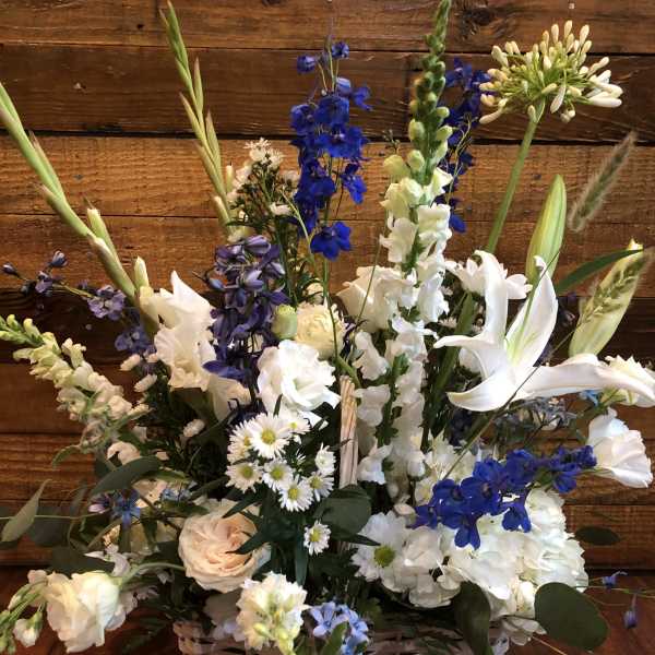 Tall white and blue flower basket with lilies, roses, daisies, hydrangeas, and delphinium in a white woven basket