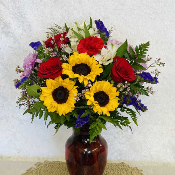 Bouquet of sunflowers, red roses, and white lilies in a glass vase