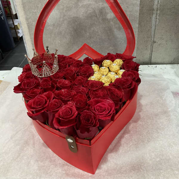 Red roses arranged in a heart-shaped gift box with gold chocolates and a jeweled crown