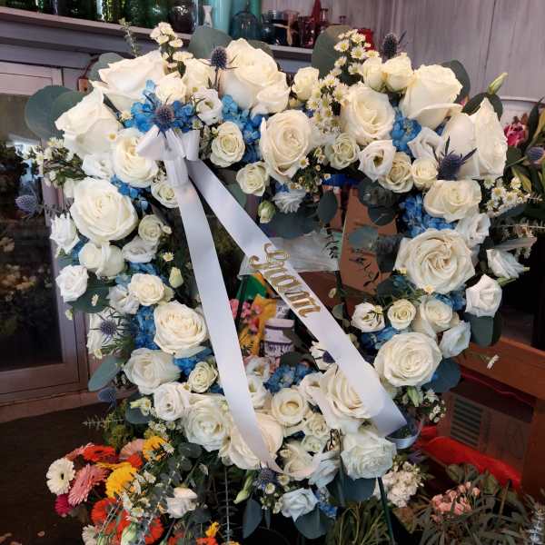 Heart-shaped wreath of white roses with blue flowers and a white ribbon