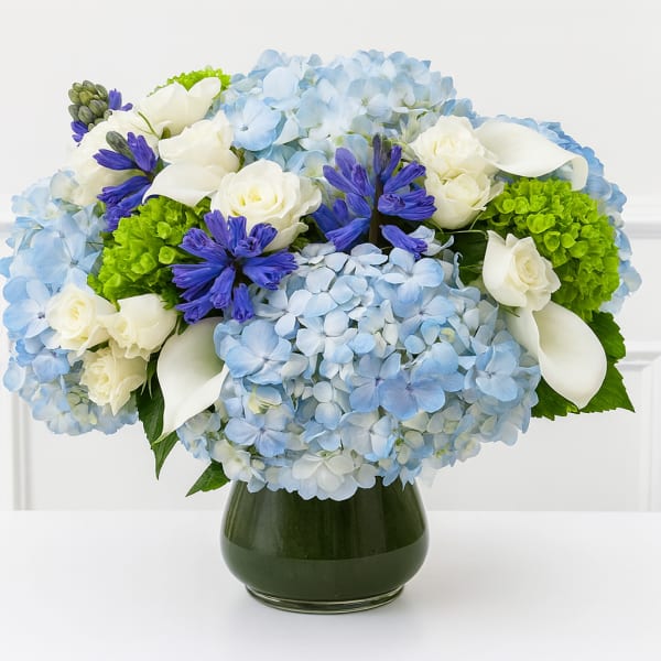 Blue hydrangeas with white roses and purple flowers in a dark glass vase