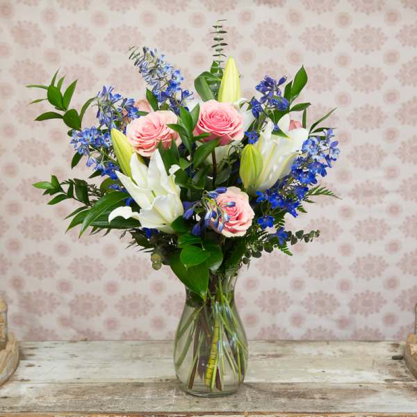 Pink roses and white lilies in a clear glass vase with blue flowers