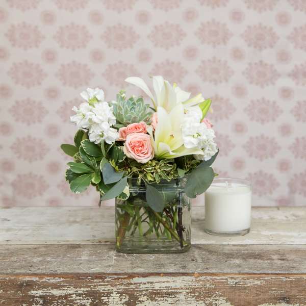 Pink roses and white lilies arranged in a glass vase beside a white candle.