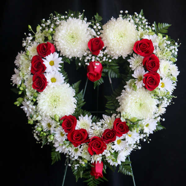 Heart-shaped floral wreath with red roses and white flowers on a stand