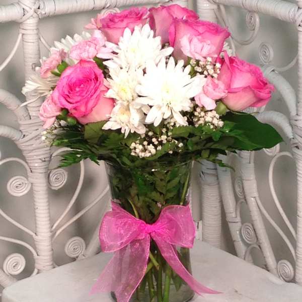 Pink roses and white daisies in a glass vase with a pink ribbon