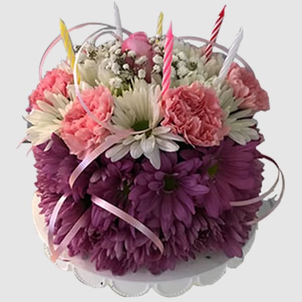 Pink and purple flower arrangement with striped candles in a white container