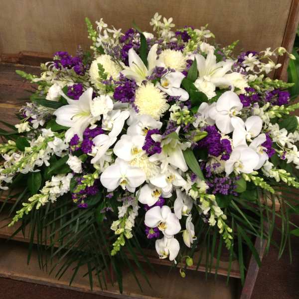 White orchids and lilies arranged with purple flowers in a low spray.