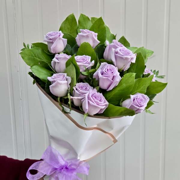 Bouquet of lavender roses wrapped in white paper with a purple ribbon