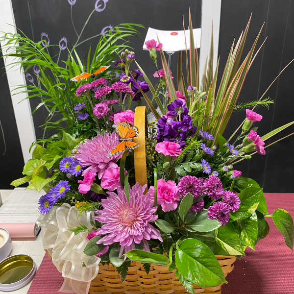 Basket arrangement of pink and purple flowers with butterflies and a ribbon bow