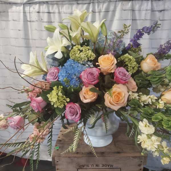 Large mixed bouquet with roses, lilies, hydrangeas, and delphinium in a white vase