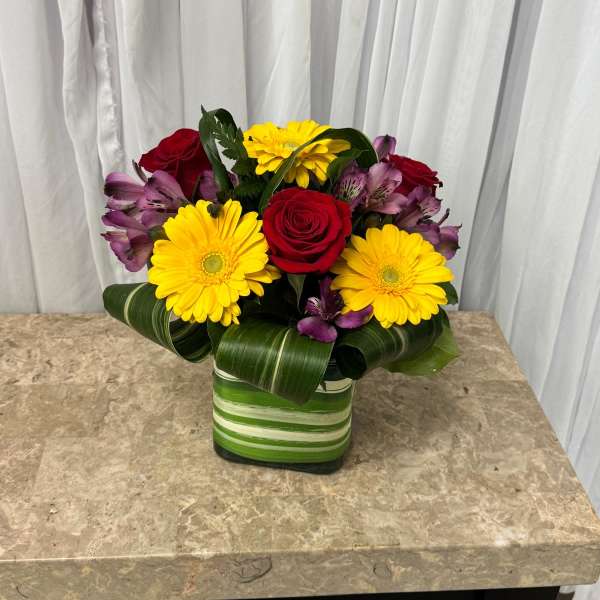 Red roses, yellow gerberas, and purple alstroemeria in a striped vase