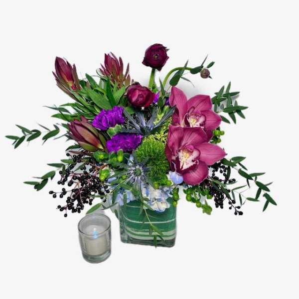Purple floral arrangement in a square glass vase with a small candle
