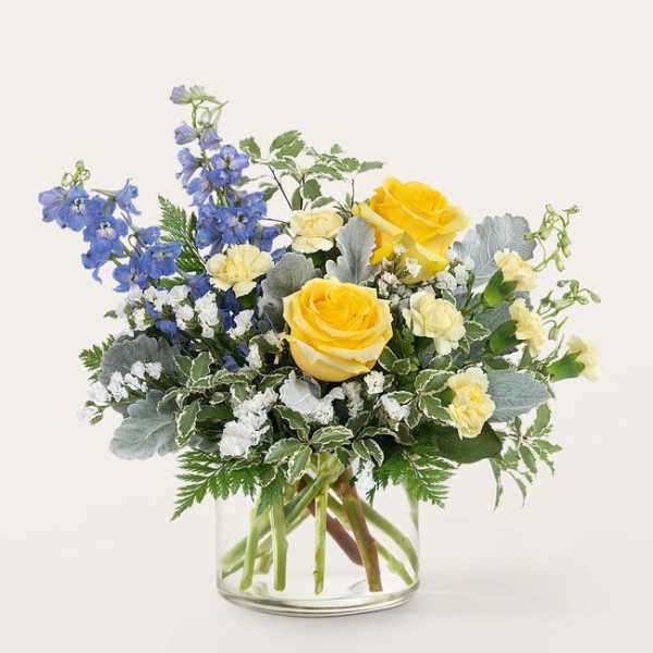 Yellow roses and blue delphinium in a clear glass vase