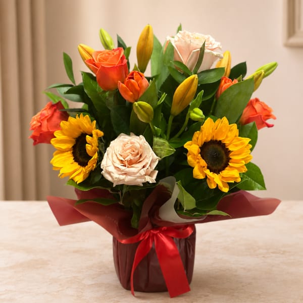 Bouquet of roses, sunflowers, and tulips in a wrapped vase with a red ribbon