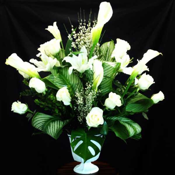 White calla lilies and roses in a white vase with large green leaves