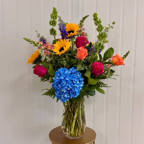 Mixed bouquet with sunflowers, roses, and blue hydrangea in a clear glass vase