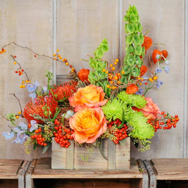 Wooden box arrangement with orange roses, green mums, and berries
