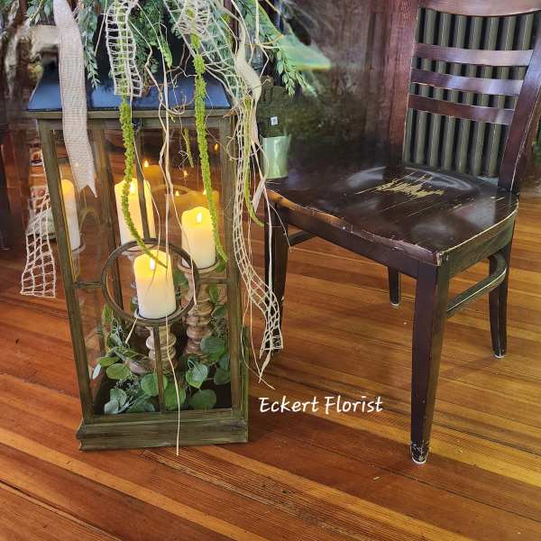 Lantern centerpiece with candles and trailing greenery on a wooden floor