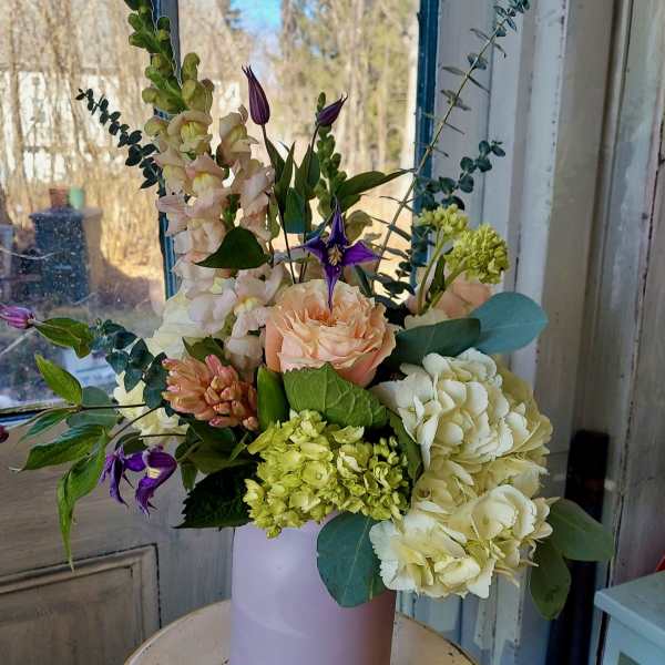 Mixed bouquet in a pale pink vase with peach, white, and purple flowers