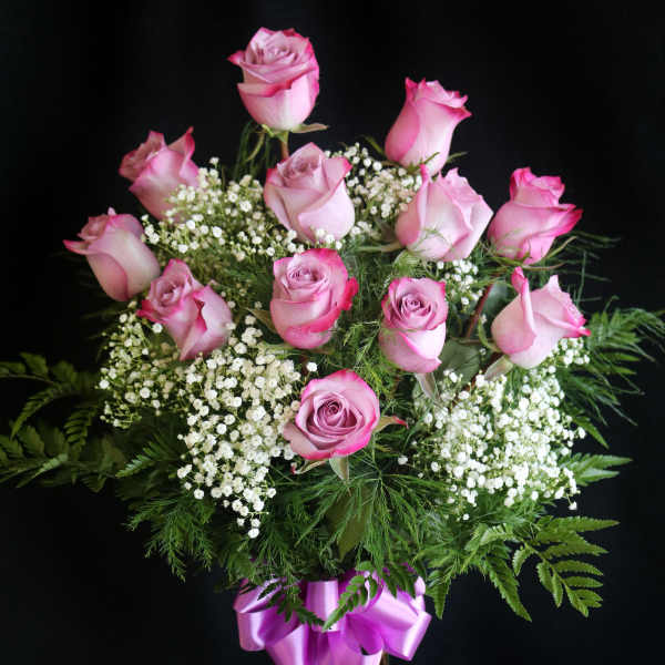 Pink roses in a glass vase with white filler flowers and a purple ribbon