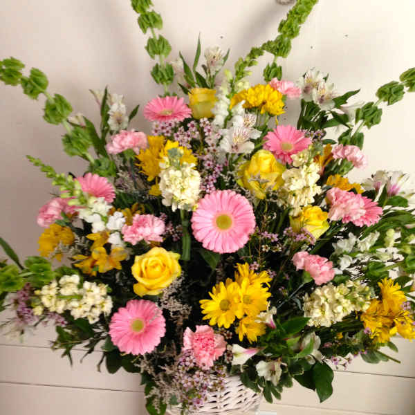 Mixed bouquet of pink and yellow flowers in a white basket vase