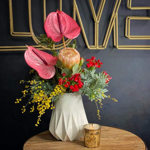 Pink anthuriums and red flowers in a white vase with yellow filler