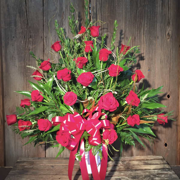 Red roses arranged in a white vase with a pink ribbon bow