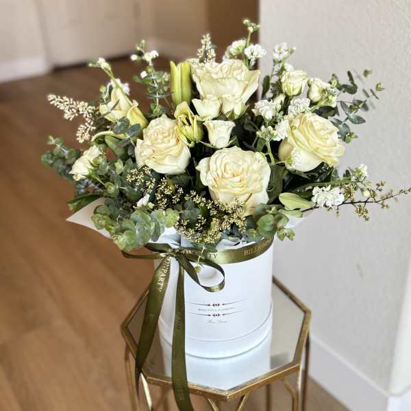 Cream roses and white blooms arranged in a white hat box with a ribbon