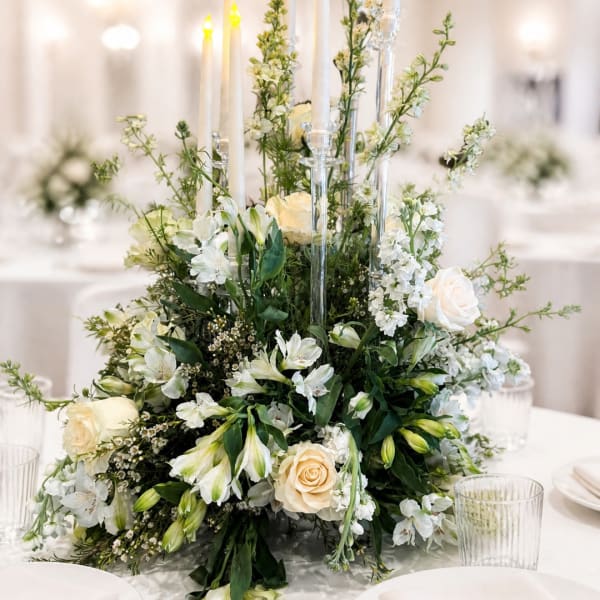 White floral centerpiece with roses and lilies around tall candles