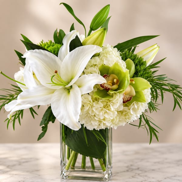 White lilies and pale green orchids in a clear glass vase