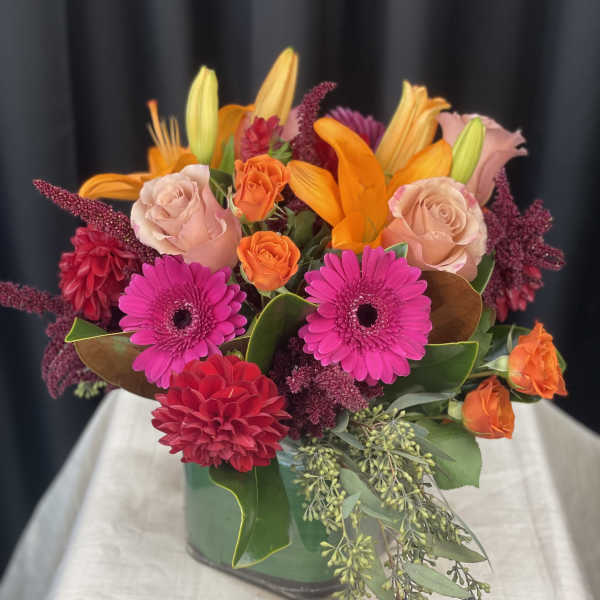 Bright mixed bouquet in a green vase with pink, orange, and red blooms