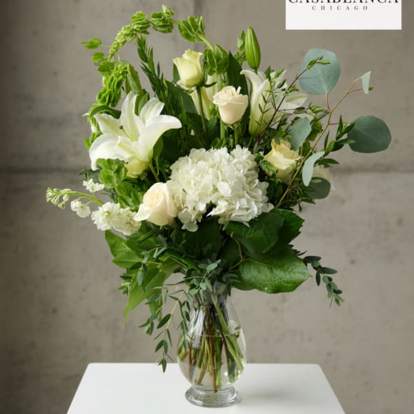 White lilies and roses in a clear glass vase with greenery