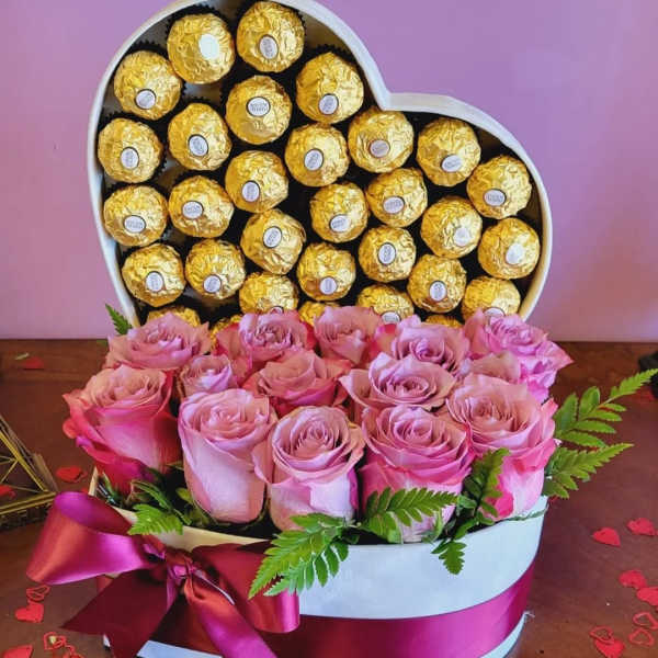 Heart-shaped box of gold-wrapped chocolates with pink roses in front
