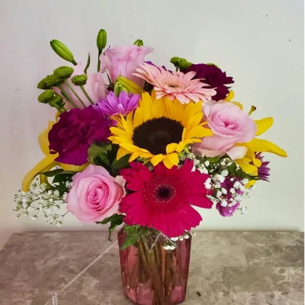 Mixed bouquet with sunflowers, gerbera daisies, roses, and lilies in a pink vase