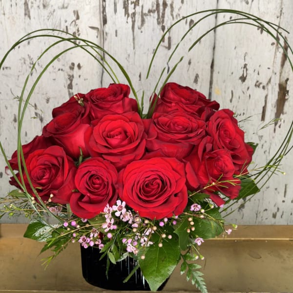 Red roses arranged in a black vase with arched grass accents