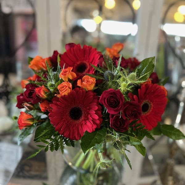 Bouquet of red gerbera daisies and orange roses in a glass vase