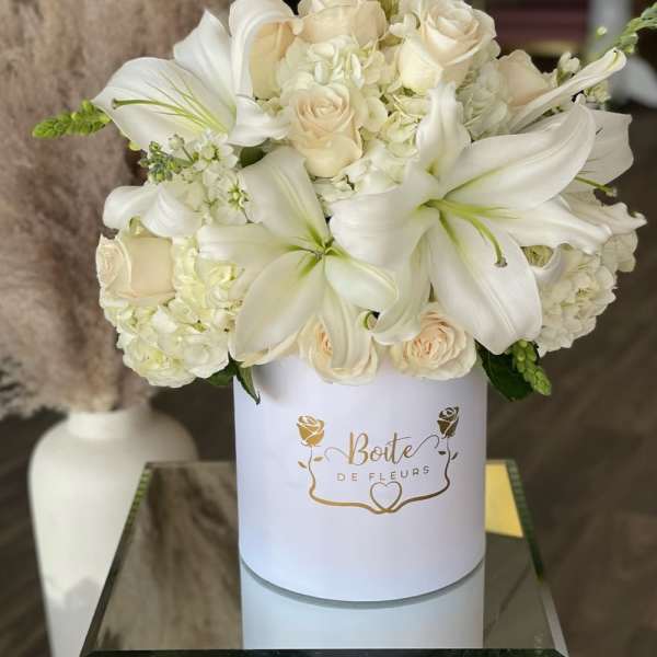 White lilies and cream roses arranged in a round white box