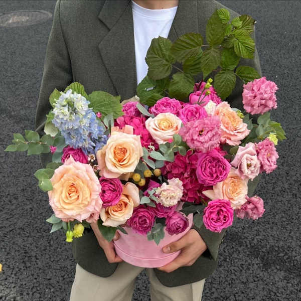 Pink and peach roses arranged in a round pink box with blue blooms