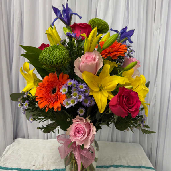 Colorful mixed bouquet in a glass vase with roses, lilies, and gerbera daisies