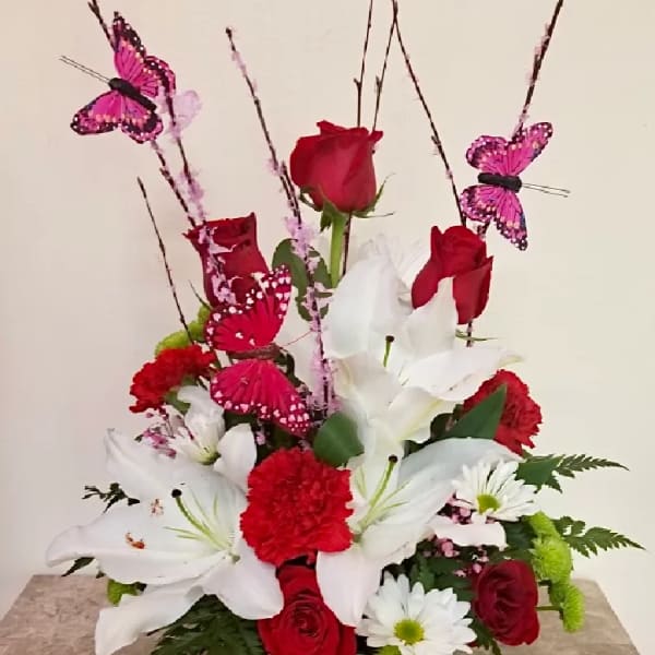 Red roses and white lilies in a white basket with pink butterfly picks