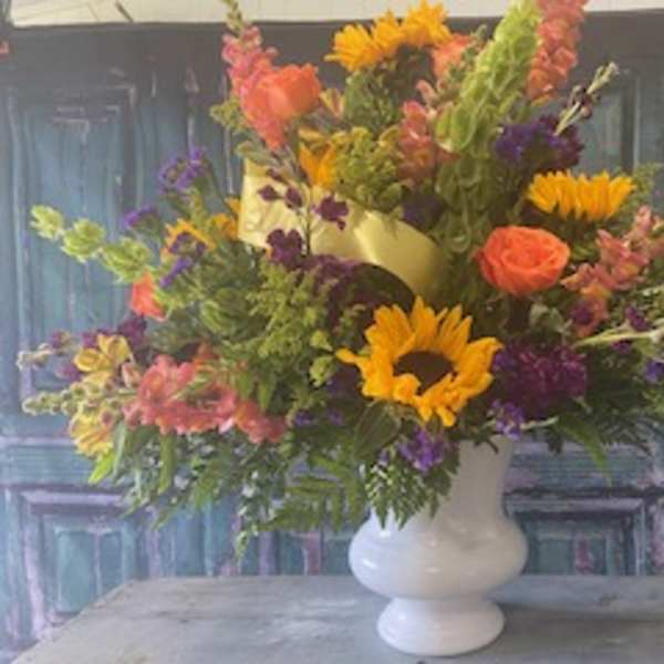 Mixed bouquet in a white vase with sunflowers, roses, and purple blooms