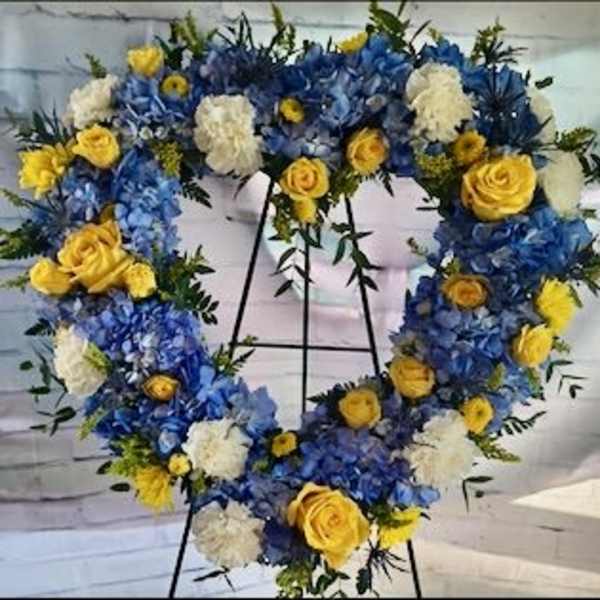 Heart-shaped floral wreath with blue, yellow, and white flowers on an easel