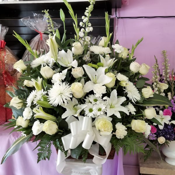 Large white floral arrangement with lilies, roses, and daisies in a basket