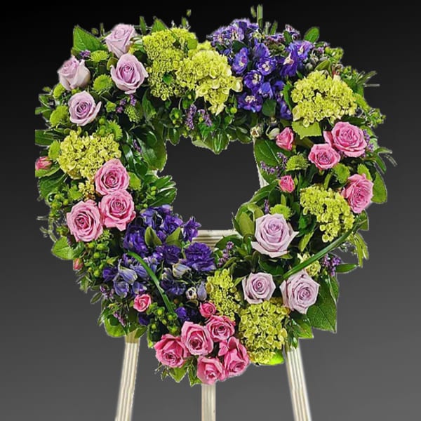Heart-shaped floral wreath with pink roses and purple blooms on an easel